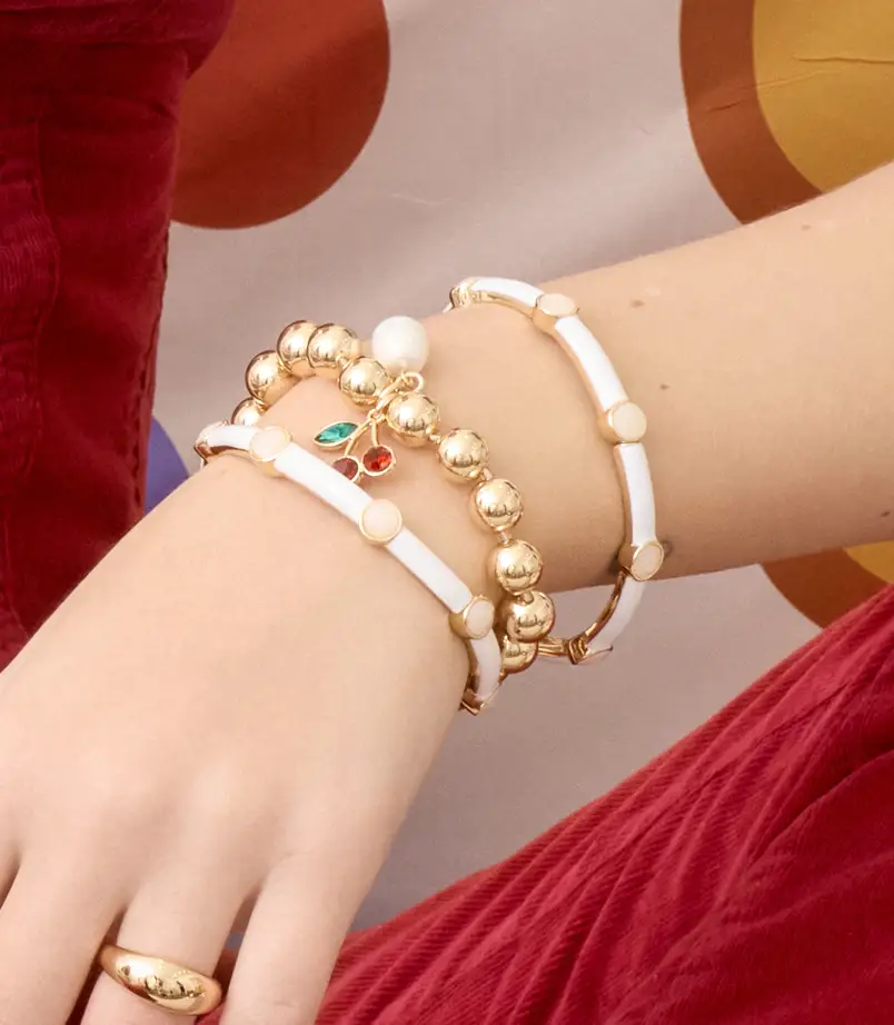 close up of 3 bracelets, gold and 3 white grouped together on a models wrist